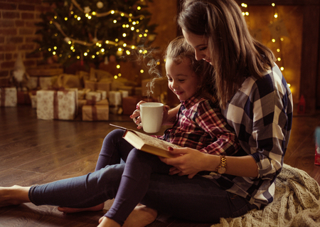 Pretty mother reading a book for her daughter in a calm, winter eveneingの写真素材