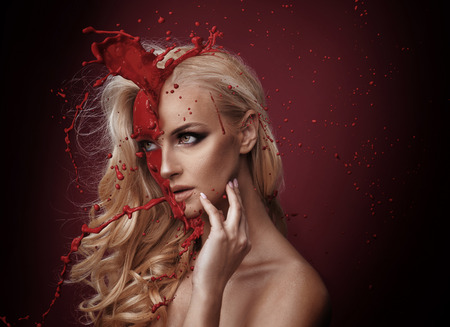 Art portrait of a pretty woman being poured over with red paintの写真素材