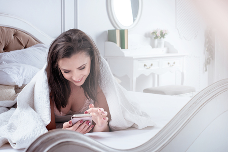 Cheerful woman relaxing and using a smartphone in an apartmentの写真素材