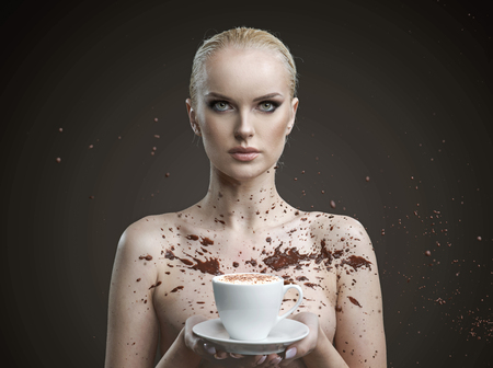 Chocolate splashing against a nude woman holding a cup of coffeeの写真素材