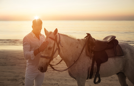 Handsome, young guy walking with a stallion alongside the coastの写真素材