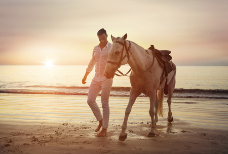 Handsome, young guy walking with a stallion alongside the coastの写真素材