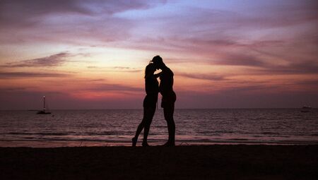 Young, relaxed couple kissing on a tropical beach, sunset in background