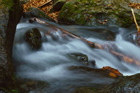 Long exposure photo of the mountain creek with rocks and leaves