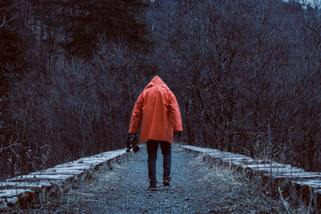 Man in orange hooded jacket with the mask in hand on the old abandoned stone railway viaduct.