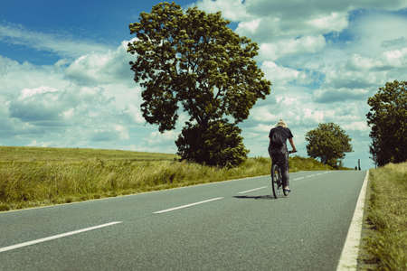 girl riding a bicycle along the asphalt road among the fields of wheatの写真素材