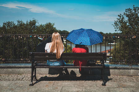 two women with umbrellas sitting on a bench on the observation deckの写真素材