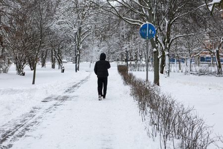 A man jogging in the park during a winter snowfall.