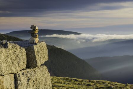Pile of stones stacked in the mountains against the backdrop of a beautiful panorama with the setting sun against the background of the sky of fog and cloudsの写真素材