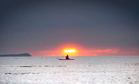 Silhouette of the girl on a surfboard at sunsetの写真素材