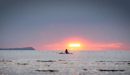 Silhouette of the girl on a surfboard at sunsetの写真素材