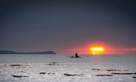 Silhouette of the girl on a surfboard at sunsetの写真素材