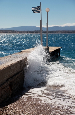 Sunlit waves on a pier on the Gulf coast in Greece  On the pier installed Greek flagの写真素材