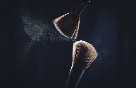 Cosmetic brush with pastel pink cosmetic powder spreading on black backgroundの写真素材