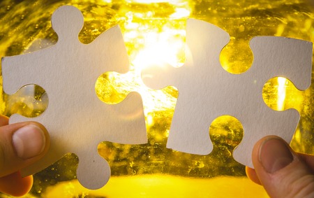 two hands trying to connect couple puzzle piece with sunset background. Jigsaw alone wooden puzzle...