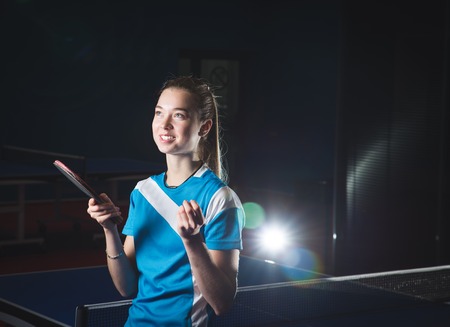 portrait of elegant attractive glamor pinup girl dazedly looking at camera posing in red dress with flower in hair & holding bat ball for table tennis on white or light copy space background closeupの写真素材