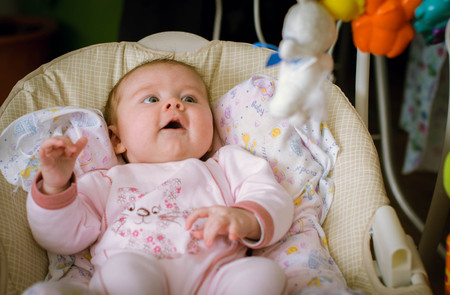 Very cute little baby boy lying on the bed at the back in the crib next to a bright toy