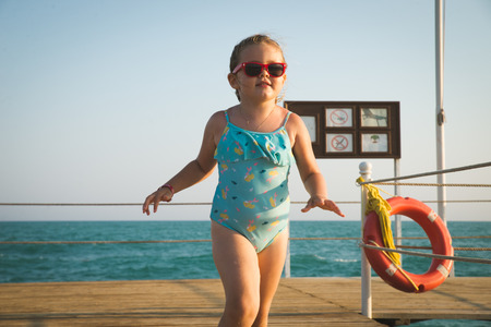 3 years old boy walking on beach wooden pier ready to swim in a sea. Summer outdoor activities with children on the beach. Blue sky and ocean in the morning. Safety first.の写真素材