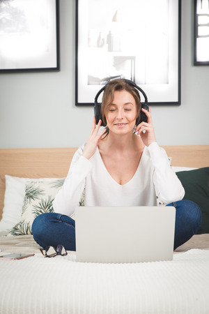 Girl in plaid listening music in headphones, sitting on sofa.の写真素材
