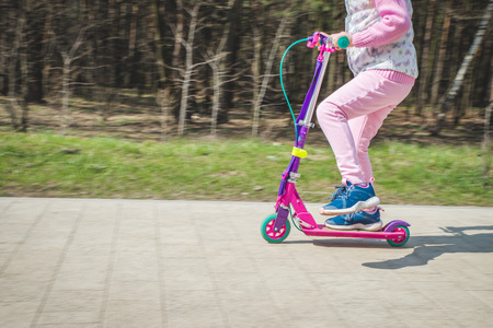 A nice little girl is riding a scooter. Active leisure on city streets. Children's sportsの写真素材