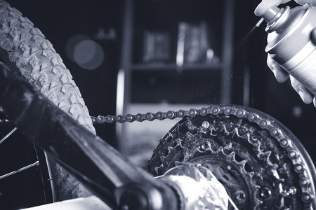 Cleaning and oiling a motorcycle chain and gear with oil Spray/dark lightの写真素材