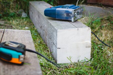 Builder cuts a sheet of plywood with an electric jigsaw and holds it with his hand.
