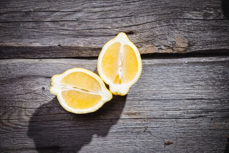 Photo of fresh ripe lemons on retro background. A slice of lemon with green leaves. Lemon fruit on wooden plate bowl. Lemon around fruits. Copy space. Grey background. Imageの写真素材