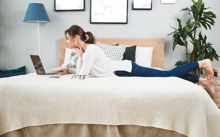 young teen girl laying on her bed in white dress and surfing the internetの写真素材