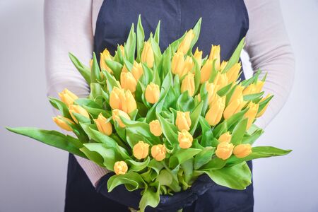 Closeup of young woman florist in apron and sneakers with two bouquets of tulips standing in flower shopの写真素材
