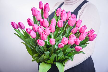 Closeup of young woman florist in apron and sneakers with two bouquets of tulips standing in flower shopの写真素材