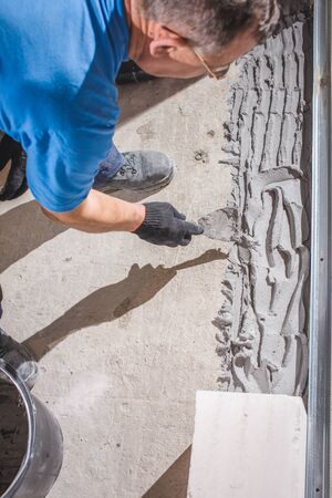 Reconstruction of the house. Worker stuck brick cladding (imitation brick) on the outside facade. Man cement is applied with a trowel.の写真素材