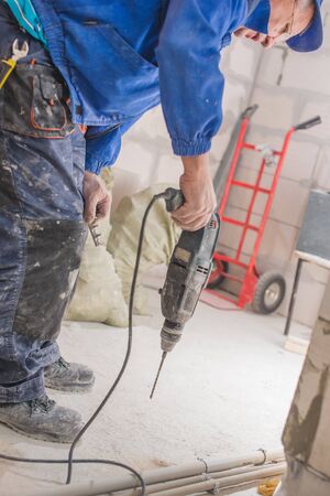 Home repair. Male hands using an electric perforator drill with a drill make a hole in the wall with peeling paint.の写真素材