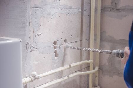 a man working in a white helmet with a large perforator drills a light wall, copy space; space for textの写真素材