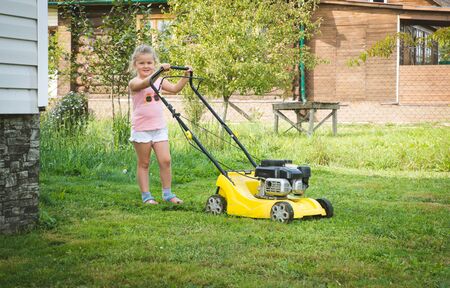 Little blond toddler boy playing with lawn mower machine in summer garden on sunny dayの写真素材