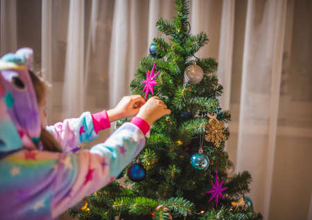 little girl dressed up as a reindeer Rudolf decorating a Christmas treeの写真素材