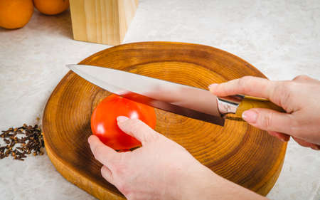 Woman's hands cutting tomato, behind fresh vegetables.