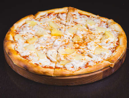 Tasty hawaiian pizza with chicken and pineapple on wooden cutting boardの写真素材