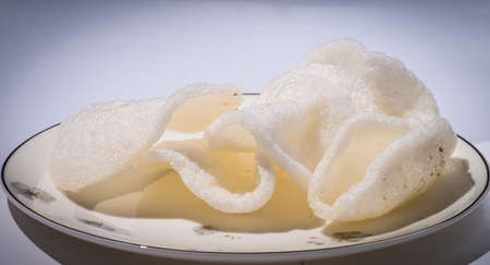 Pile of white fried rice chips on the brown dish on a white background, close-upの写真素材