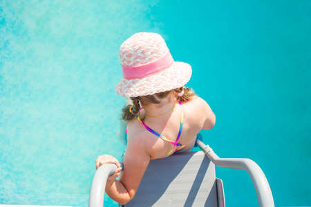 A child in goggles on the steps climbing out of the pool, little girl having fun in the swimming pool, summer vacation at home, tropical holiday resort.の写真素材