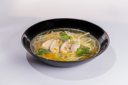 Chicken noodle soup with parsley and vegetables in a white plate, gray background.の写真素材