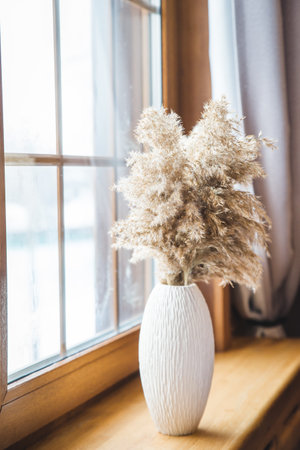 A minimalistic bouquet of white tulips, pink eustoma, hyacinth, eucalyptus in a fluted glass vase on a white panel of an artificial fireplace. Cup of tea, faience figurines of a two birdsの写真素材