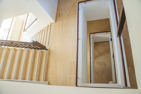 Hotel staircase with slightly curved architecture, windows and historic metal railing. Stairs are tiled and the handrail is supplemented with wooden handrail. There is also wood on walls and paneling.の写真素材