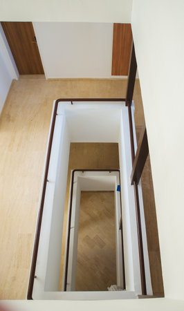 Hotel staircase with slightly curved architecture, windows and historic metal railing. Stairs are tiled and the handrail is supplemented with wooden handrail. There is also wood on walls and paneling.の写真素材
