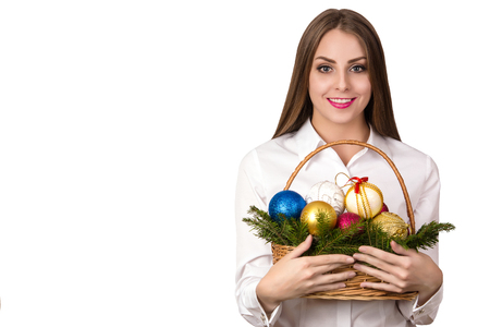Beautiful European young happy woman with healthy skin and charming smile in white shirt with basket of Christmas decorationsの写真素材