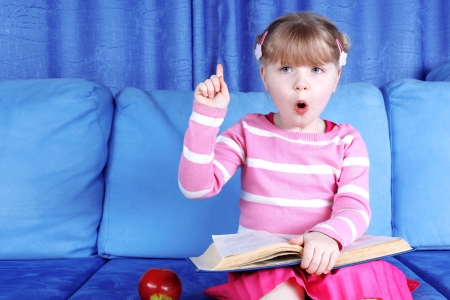 surprised little girl with apple and books in sofaの写真素材
