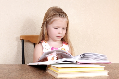 Little girl reading book in the kitchen against yellow wall at homeの写真素材