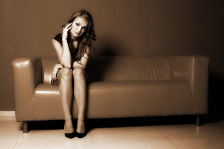 Beautiful woman seated on a orange sofaの写真素材
