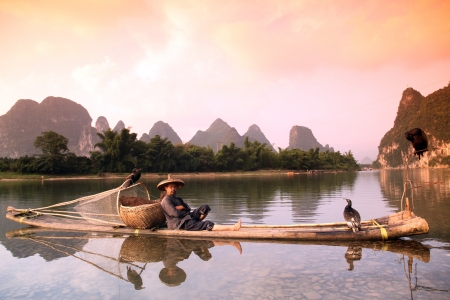YANGSHUO - JUNE 18: Chinese man fishing with cormorants birds in Yangshuo, Guangxi region, traditional fishing use trained cormorants to fish, June 18, 2012 Yangshuo in Guangxi, Chinaのeditorial素材