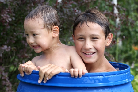 Two boys 3 and 10 years old in barrel in water in hot summertime dayの写真素材