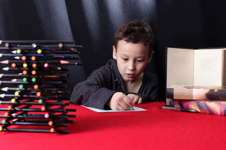 The boy writes and studies at the table with books and pencilsの写真素材
